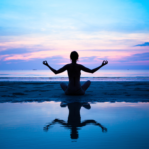 Radical Self-Care - Woman enjoying a peaceful meditation at the beach during sunrise.